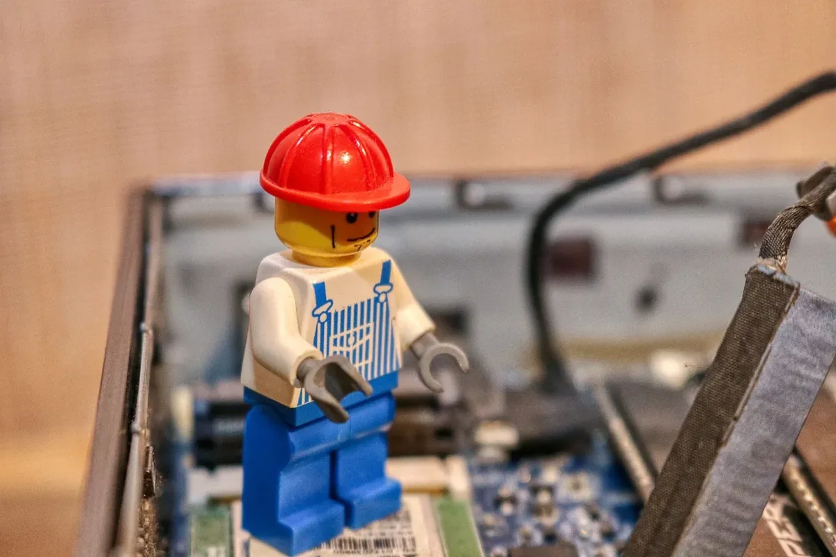 A Lego workman in a red hard hat standing inside an opened laptop, among the circuit boards.